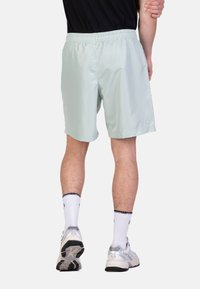 Pantaloni corti sportivi verde chiaro con cintura elastica, materiale in poliestere e tasche laterali, abbinati a calzini bianchi e scarpe da corsa.