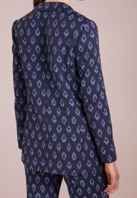 Marinblå blazer i texturerat tyg med ett ljusblått diamantmönster och en skräddarsydd passform, inklusive en uppklippt slagkrage och axelvaddering.