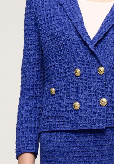 Jachetă texturată bleu cu un design cu două rânduri de nasturi, având nasturi aurii, guler tăiat și un material moale țesut.