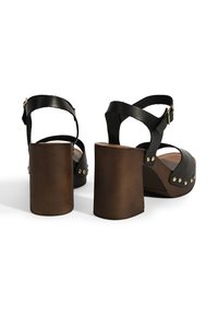 Zwarte leren platformsandalen met een stevige bruine hak, voorzien van een bandjesontwerp, gouden studs en een verstelbare enkelband.