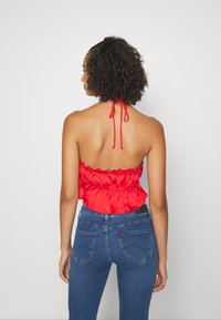 Top cropped de cetim vermelho com bainha em babados e alças ajustáveis, combinado com jeans justos de tom azul escuro com bolsos traseiros e costura discreta.