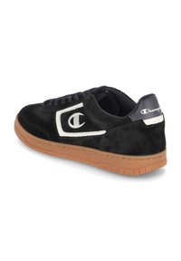 Adidași negri din suede cu un logo alb în contrast, talpă din cauciuc bej și șireturi negre. Partea din spate prezintă un accent alb pe călcâi cu detaliul logo-ului.
