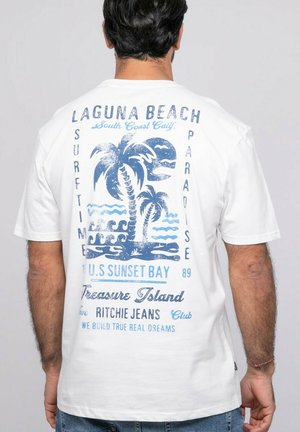 Homme portant un t-shirt blanc avec un motif de palmier bleu et une vague, comportant un texte sur Laguna Beach, le surf et Treasure Island.