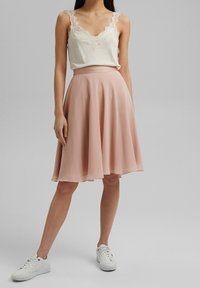 Lätt, ljusrosa kjol med utsvängd design, kombinerad med en krämfärgad linne med spetsdetaljer längs halsringningen. Vita sneakers.