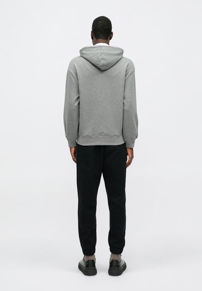 Felpa grigia con cappuccio e vestibilità comoda, abbinata a pantaloni jogger neri. L'outfit presenta polsini a costine e un design semplice e minimalista.