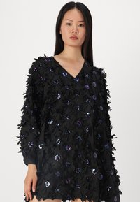 Vestido de tecido preto com decote em V, mangas longas e apliques florais texturizados com lantejoulas em várias cores por toda a peça.