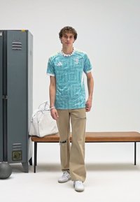 Tyrkysové sportovní tričko s mramorovým vzorem, bílými akcenty a logem; doplněné o světle béžové široké nohavice s dírami.