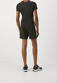 Black t-shirt with cut-out detailing and black athletic shorts with white stripes on the side, paired with black athletic shoes.