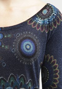 Langärmliger Pullover aus dunkelblauem, glitzerndem Stoff, verziert mit bunten, runden und floralen Mustern, akzentuiert durch Pailletten auf den Schultern.