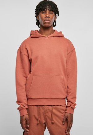 Haut à capuche couleur rouille en tissu doux avec une poche avant, coupe décontractée et capuche à cordon réglable. Associé à un pantalon assorti.
