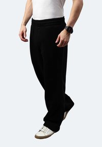 Schwarze Sweatpants aus weichem Stoff, mit einem gerafften elastischen Bund, geradem Bein-Design und einem männlichen Model, das weiße Sneakers trägt.