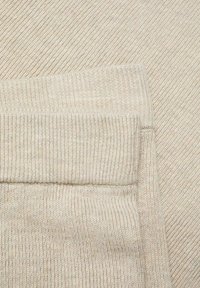 Light beige ribbed fabric showing a textured pattern. The material is soft with elastic cuffs, highlighting a casual and comfortable design.