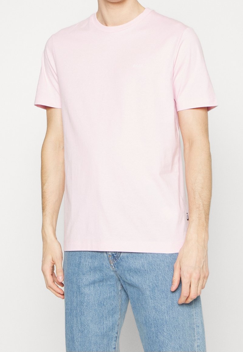 Light pink cotton t-shirt with a crew neck, short sleeves, and a small logo detail. Paired with blue denim jeans.