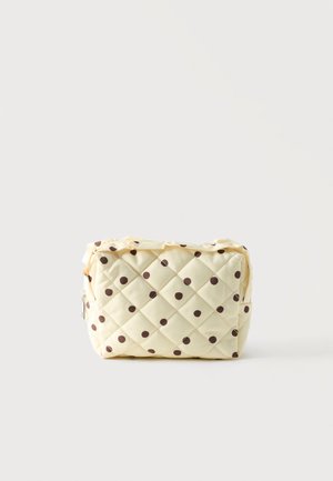 Petit sac matelassé crème avec des pois marron, forme rectangulaire, et fermeture éclair, présenté sur un fond blanc uni.