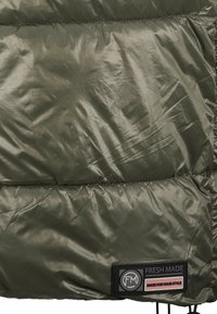 Tissu matelassé vert olive avec des coutures et une étiquette noire portant l'inscription "FRESH MADE" et "MADE FOR YOUR STYLE" au bord inférieur.