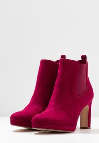 Botas de tobillo de ante fucsia con una textura suave, que cuentan con un tacón cuadrado, paneles laterales elásticos y un diseño sin cordones para facilitar su uso.