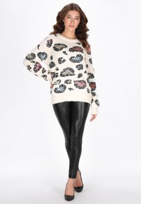 Kremowy sweter z czarnymi, niebieskimi i czerwonymi cekinowymi plamami w panterkę; luźny krój. Połączony z błyszczącymi czarnymi legginsami i czarnymi szpilkami.