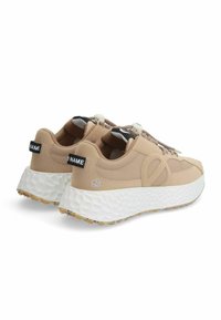 Beige sneakers met gestructureerde stof, witte gevoerde buitenzool en een uniek vetersysteem. De achterkant heeft een zwart label met 'NAAM'.