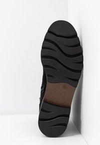 Sole di scarpa nera, testurizzata con scanalature orizzontali e curve. Il materiale sembra gommoso, con un accento marrone alla base e indicazione della taglia.