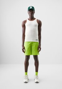 White textured tank top with multicolored trim, bright green shorts, and matching high socks. White sneakers with a textured finish. Green cap.