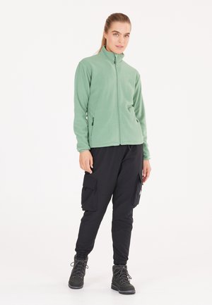 Fleecejacke in Hellgrün mit hohem Kragen und Reißverschluss, kombiniert mit schwarzen Cargo-Hosen mit mehreren Taschen und elastischen Bündchen.