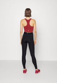 Röd racerback sporttop i kombination med högmidjade svarta leggings och rosa sportskor. Slät tyg, figurnära stil och minimal varumärkning.