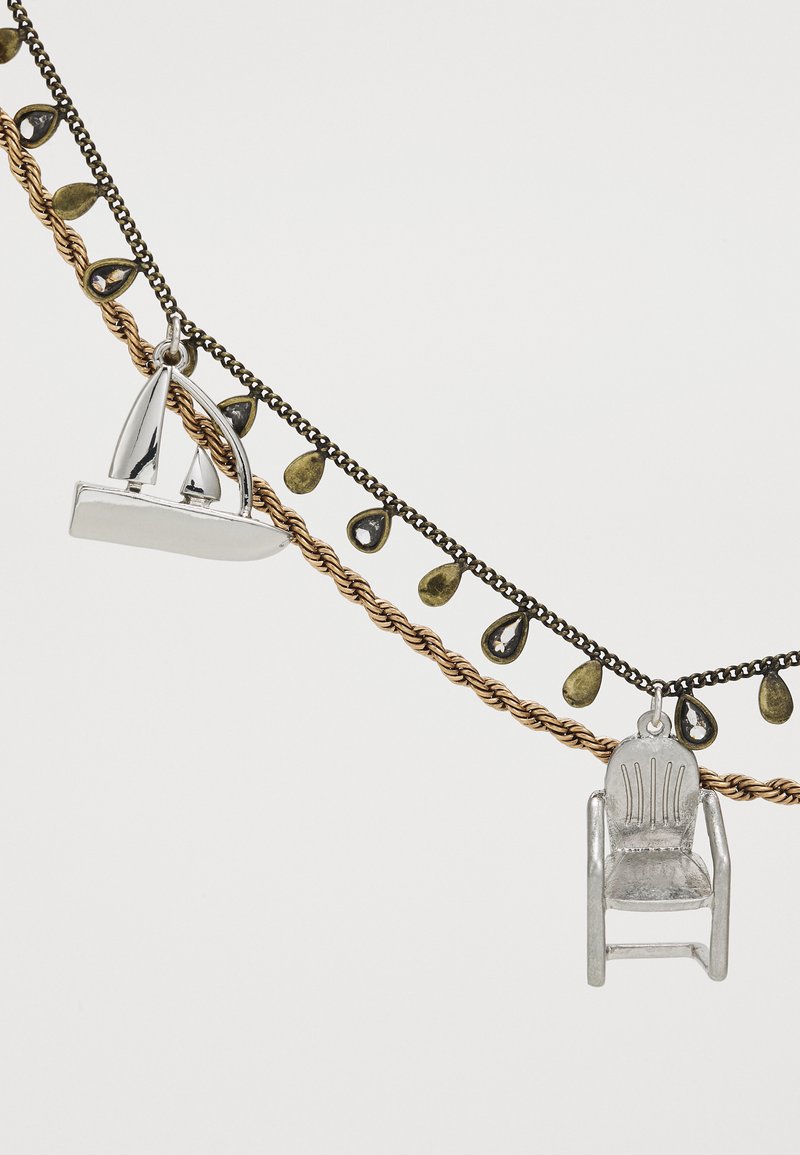 Collar de plata con un colgante de barco y silla, sobre una cadena de metales mixtos con acentos en forma de lágrima dorada y oscura.