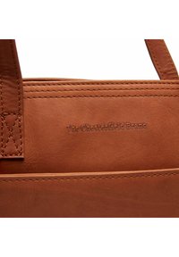 Borsa a tracolla in pelle marrone con dettagli cuciti e logo impresso. Texture liscia e forma strutturata, con due manici robusti.
