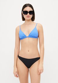Triangolo di bikini blu a costine con spalline sottili, abbinato a uno slip bikini nero uniforme. Texture liscia, design minimal.