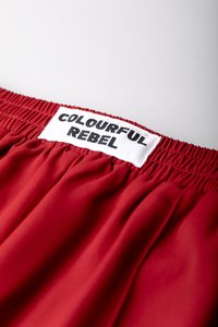 Röda shorts med elastisk midja, tillverkade av ett slätt tyg, med en vit etikett där det står "COLOURFUL REBEL" i fet svart text på midjan.