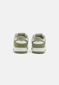 Zielone trampki Nike z fakturowanym zwierzęcym wzorem z tyłu, białymi akcentami, wyściełanym kołnierzem i grubą gumową podeszwą.