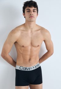 Zwarte boxershorts met een grijze Calvin Klein tailleband. De stof lijkt glad, met een slim-fit ontwerp dat de lichaamsvorm accentueert.