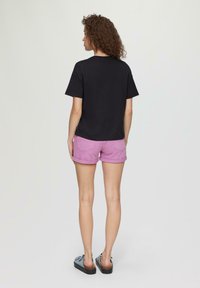 Black cotton t-shirt and pink denim shorts with rolled cuffs. Displaying a plain design. Worn with blue sandals featuring a bow detail.