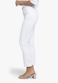 Witte denim jeans met een rechte pijpdesign, voorzien van achterzakken en details van zilverhardware, gecombineerd met versierde beige sandalen.