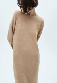Beige stickad klänning med rund hals, sänkt axel och avslappnad passform. Mjuk textur och medellång design.