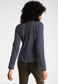 Haut à manches longues rayé bleu marine et blanc, fabriqué en tissu doux, avec une silhouette ajustée et un col rond, présentant un détail de couture au dos.