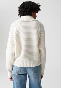 Maglione a righe crema con colletto ampio e orlo a coste, abbinato a jeans in denim azzurro chiaro. Texture morbida e vestibilità rilassata.