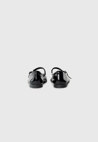 Black patent leather shoes with a low heel and ankle strap, featuring a smooth texture and rounded toe design. No notable patterns.