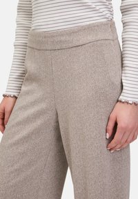 Housut, joissa on beige kalanruotokuvio, sileä pinta ja leveät lahkeet. Varustettu istuvalla vyötäröosalla ja huomaamattomilla sivusaumadetaleilla.