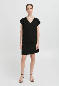 Top in lino nero con scollatura a V e maniche corte, abbinato a una gonna coordinata. Tessuto liscio, design minimal e sandali con cinturino alla caviglia.