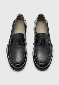 Black leather loafers with a textured surface and glossy accent. Features a round toe and a low, thick sole for comfort.