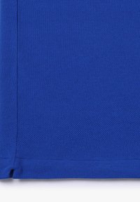 Gros plan d'un tissu bleu texturé avec des coutures visibles et un ourlet en bas.
