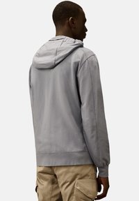 Lichtgrijze hoodie van een zachte, gestructureerde stof, met een trekkoordkap, ribgebreide boorden en een relaxed fit. Achteraanzicht weergegeven.