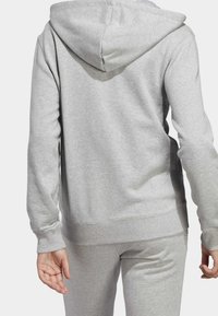 Šedá mikina s kapucí vyrobená z měkké látky, se přední klokaní kapsou, žebrovanými manžetami a kapucí. Nosená s odpovídajícími kalhotami.