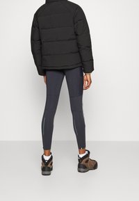 Svart pufferjacka, figursydd marinblå tights med paneler och bruna vandringskängor. Tightsen har ljusblå detaljer och texturerad design.