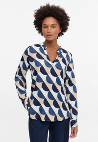 Langärmlige Bluse mit einem geometrischen Muster in Marineblau, Beige und Hellgrün. Leichter Stoff mit einem V-Ausschnitt und lockerer Passform.