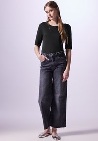 Svart åtsittande topp med korta ärmar, matchad med högmidjade, vida mörkgrå jeans. Silverfärgade ballerinaskor med en glänsande yta fulländar outfiten.