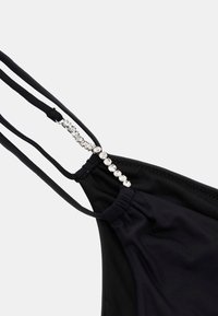 Melna bikini augšdaļa ar plāniem siksniņām un dekoratīviem kristālu akcentiem pa vidu. Izgatavota no elastīga materiāla ar savilkta sāniem.
