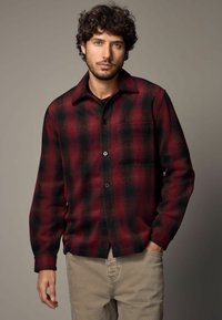 Veste chemise à carreaux rouge et noir en tissu doux, dotée d'une fermeture à boutons, d'une poche poitrine et de longues manches avec des poignets à boutons.