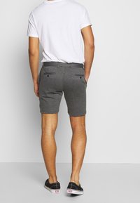 Pantaloni corti grigi realizzati in un tessuto testurizzato, dotati di due tasche posteriori, passante per cintura e un design frontale piatto, abbinati a una maglietta bianca semplice.